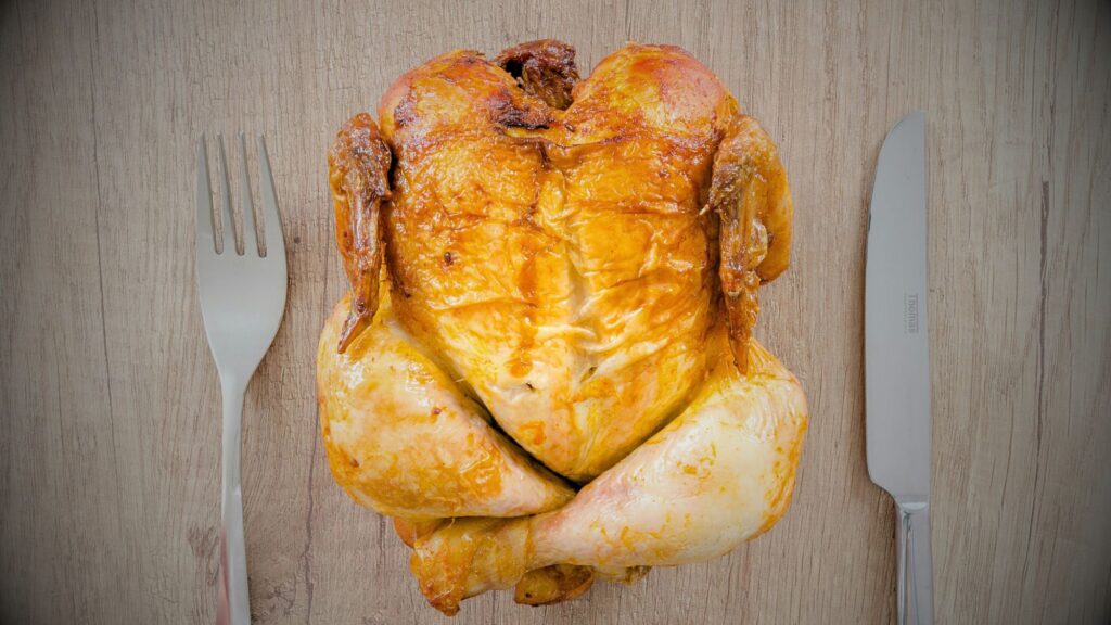 A chicken, the favorite meat, perched on a table with a knife and fork, ready to be served