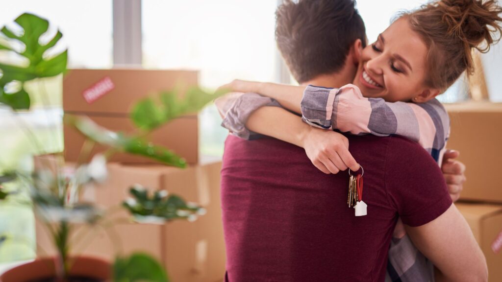 A couple embraces in front of a moving box, symbolizing the excitement of moving and settling into a new house