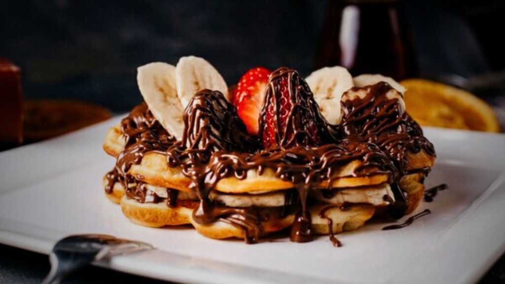 A delicious popular dessert of waffle adorned with sliced bananas and drizzled with rich chocolate sauce