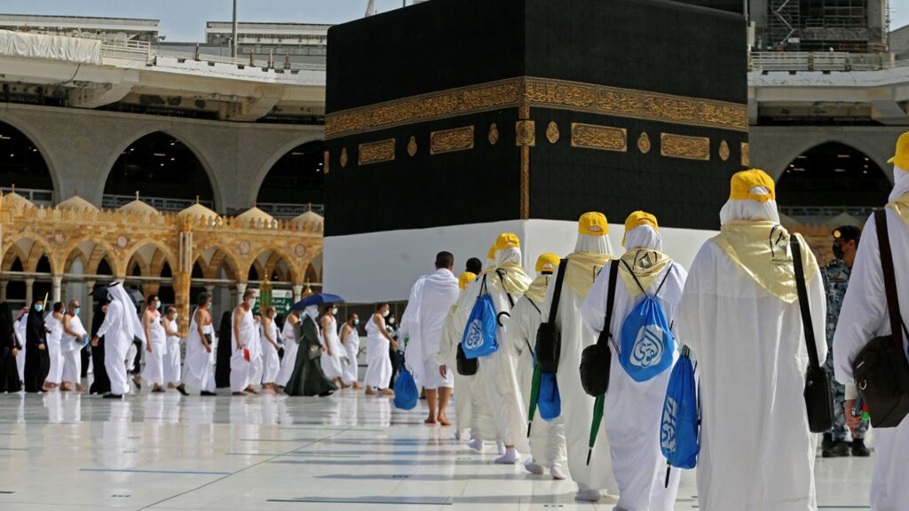 People in white robes and hats standing around the Kaaba during Umrah deals